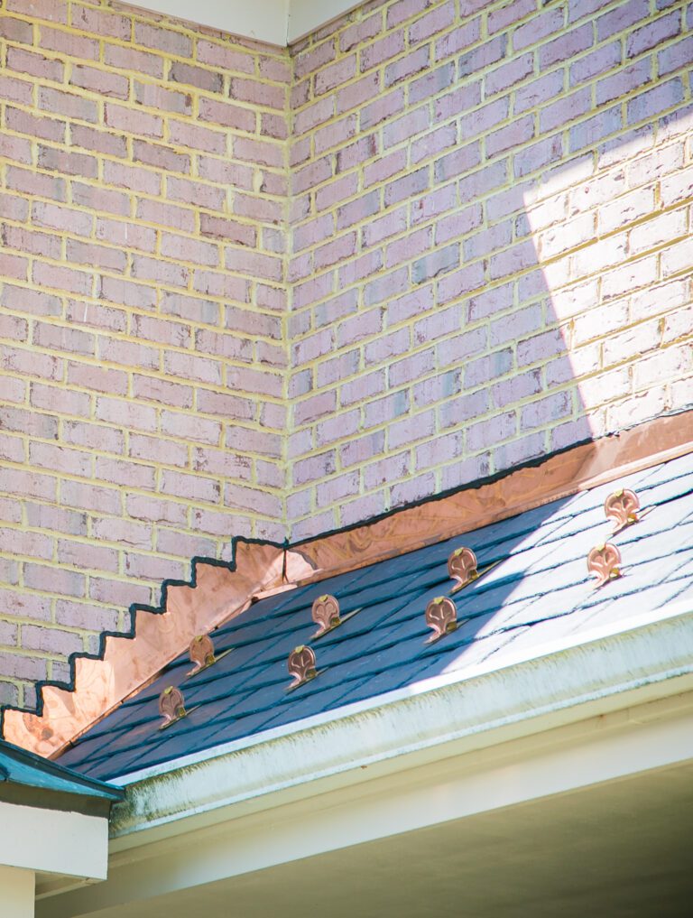 This image is of custom copper step flashing along a light brick home in Avenel. The home owner choose to go with natural non-fading black slate and copper snow guards.