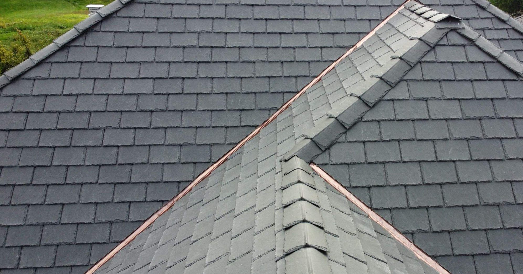 This photo is of a gray synthetic slate tile roof system installed by American Custom Contractors. The drone photo was taken on a sunny day along crown the roofline