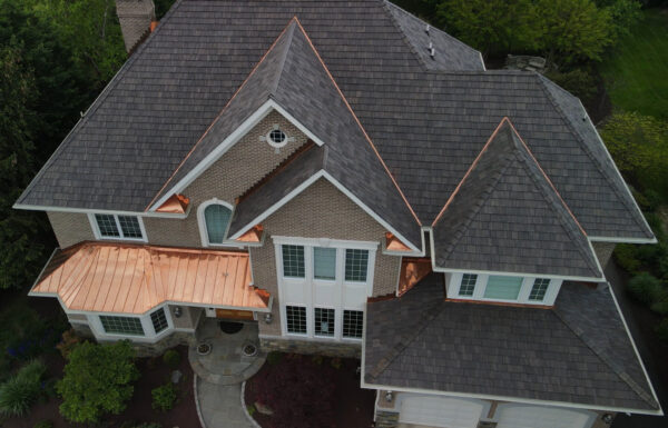 A birds eye view of a large brick front home with a synthetic cedar roofing system installed. Accented by a standing seam copper accent roof and copper valleys.