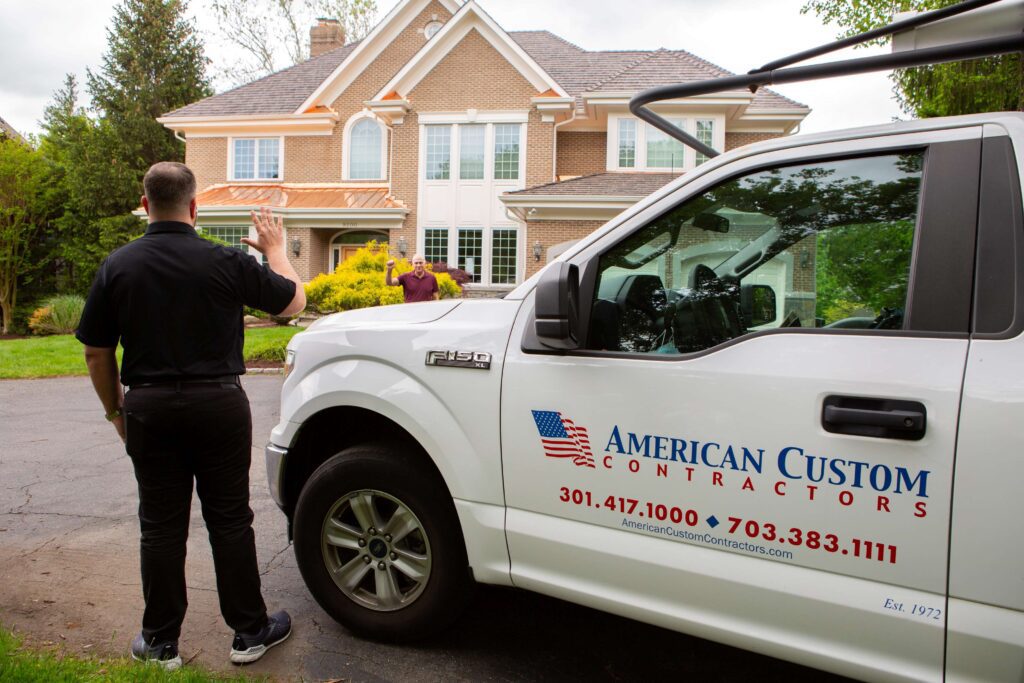 American Custom Contractors truck parked outside a customer's large brick home. The owner of the company is waiving to the homeowner as he walks up.