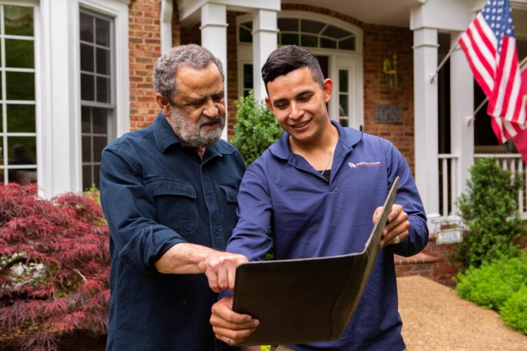 a young male project consultant speaking with a homeowner about their roofing, siding, window, and gutter projects while standing in front of his brick home in Maryland.