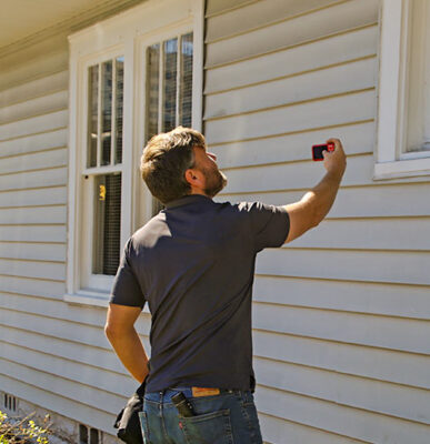 Person doing a inspection of windows and siding on a house