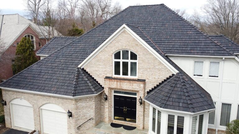 This image is a drone photo of the top level of a large home in Potomac Maryland. It features a blond stone home with a Brava Synthetic Cedar Shake roof system installed by American Custom Contractors. The photo was taken in a sunny day.