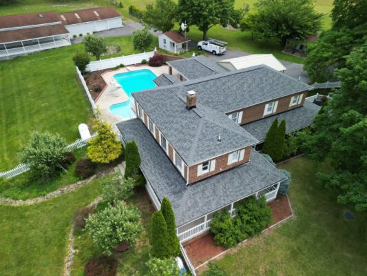 Drone photo of a home in Hagerstown, Maryland taken on a sunny day. Home is a 2 story brick home with a big bright blue pool in the back.  The roof is newly installed Owens Corning Estate Gray shingle.