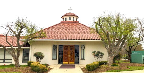 Greek Orthodox Church in Bethesda Maryland. Traditional Spanish-style cream-colored stucco building with red clay Spanish tiles and a solid wood door.