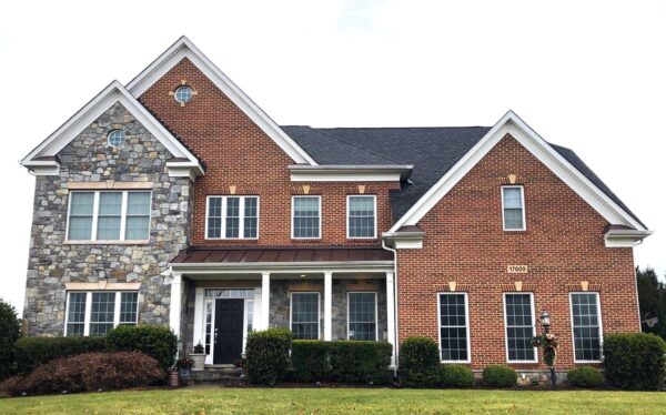 Large red brick & stone Maryland house facade with a new black asphalt shingle roof. The photo was taken on a cloudy day in Poolesville, Maryland.