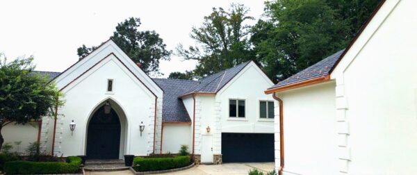 White Spanish-style home with synthetic slate roofing tiles, copper gutters and downspouts.