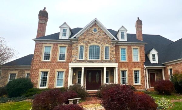 Large brick & stone Maryland house facade with a new black asphalt shingle roof. The photo was taken on a cloudy day.