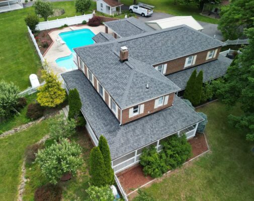 Drone photo of a home in Hagerstown, Maryland taken on a sunny day. Home is a 2 story brick home with a big bright blue pool in the back. This homeowner called us for roofing services because off a leak. The roof shingles installed were Owens Corning in the color Estate Gray