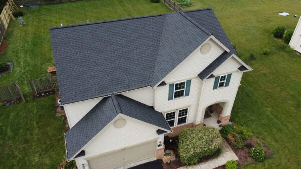 White farmhouse style home set in a rural setting. This drone photo focuses on the new charcoal color asphalt shingle roof.