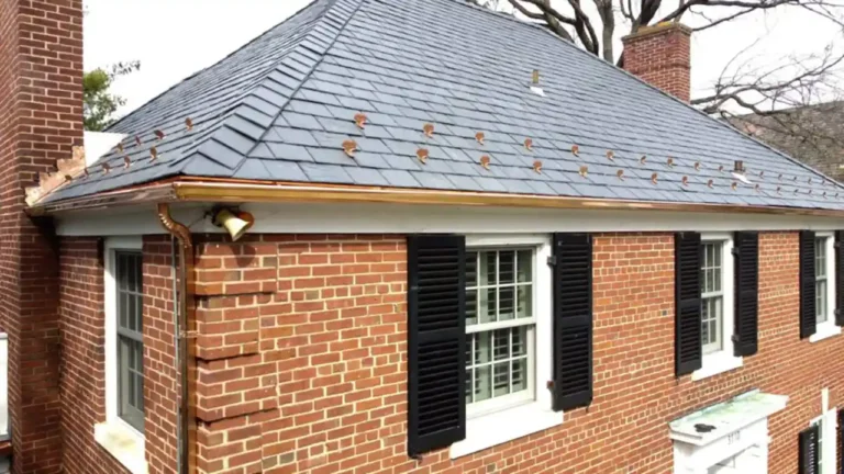 Drone picture of a large red brick home. The angle of the photo is on the 2nd-floor corner. This showcases the gleaming custom copper gutter system. The home also features a natural slate tile roof with copper snow guards around the edge.