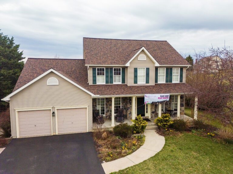 This 2 story home in Middletown, MD just recieved a refresh with a new Owens Corning Asphalt roof system in Brownwood. The photos features the finished home with light brown vinyl siding and green shutters. The phot was taken on a cloudy day and the grass is nice and green.