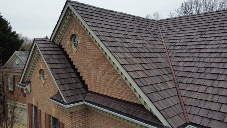 Close-up view of a rooftop installed with Brava Synthetic Cedar Shake tiles, featuring an integrated metal channel. The image showcases the expert craftsmanship of American Custom Contractors, with a beautifully landscaped garden and koi pond visible below.