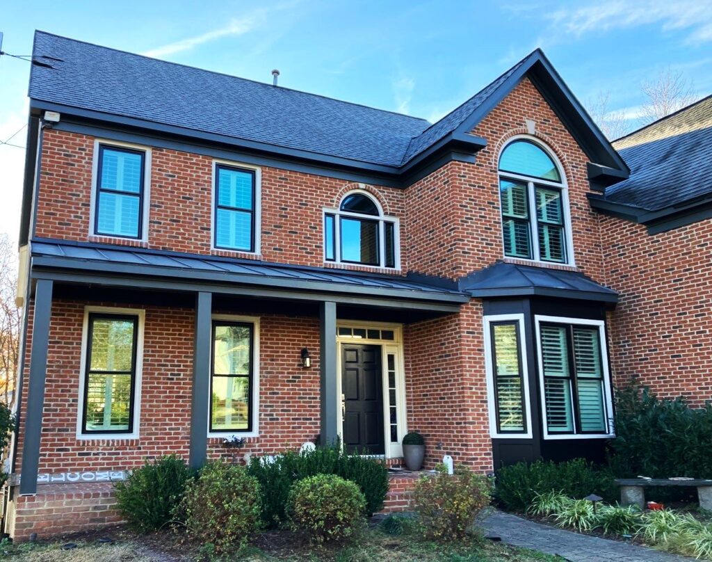 Close-up picture of the front of a red brick 2 story house featuring all new black frame Mezzo windows and doors from Alside. And American Custom Contractors installed a new custom fabricated standing seam metal roof system in the color charcoal.