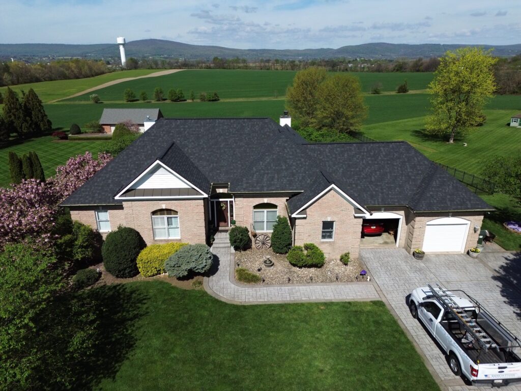 This image features a drone shot of blong brick Middletown, MD home that just recieved a upgrade from American Custom Contractors. They installed a Owens Corning Onyx Black asphalt roof system and new custom fabricated black gutter system.