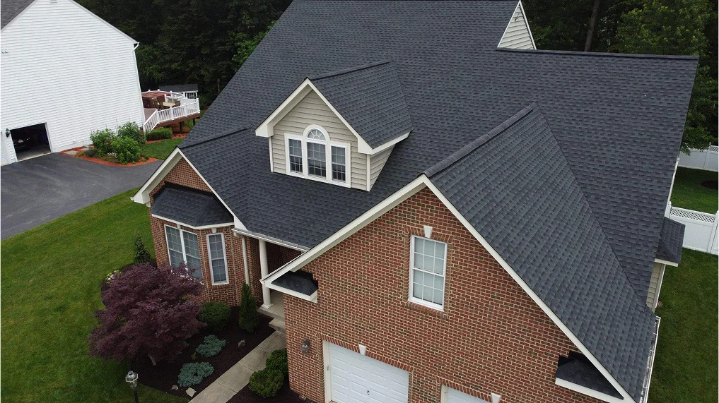 A birdseye view of a newly installed roof in Rockville, MD. The image features a 2 story red brick home with a newly installed asphalt roof by American Custom Contractor local residential roof experts in the DMV. This image show green grass surrounding the home in a residential neighborhood.