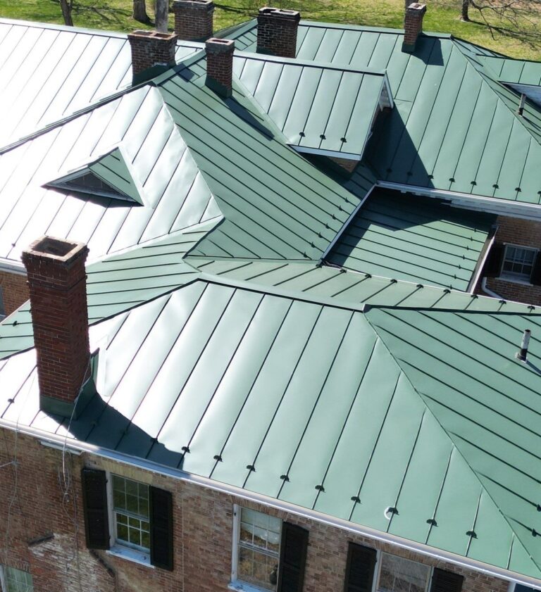 close up of a beautiful green custom-fabricated standing-seam metal roof recently installed by American Custom Contractors in Shepherdstown, WV. The sprawling home features 6 brick chimney stacks, 7 different elevations of roof, and precisely installed snow guards along the gutter line. The photo was taken on a beautiful, clear sunny day.